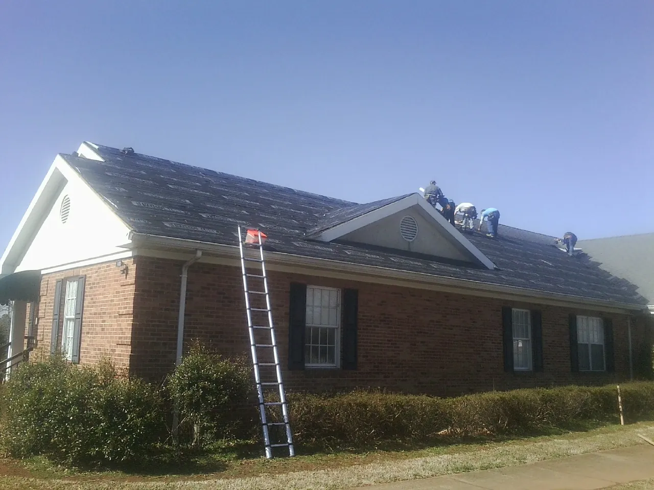 Crew tearing shingles off a brick ranch roof with a ladder set — Metal Roof Repair work by our crew in Bird Island