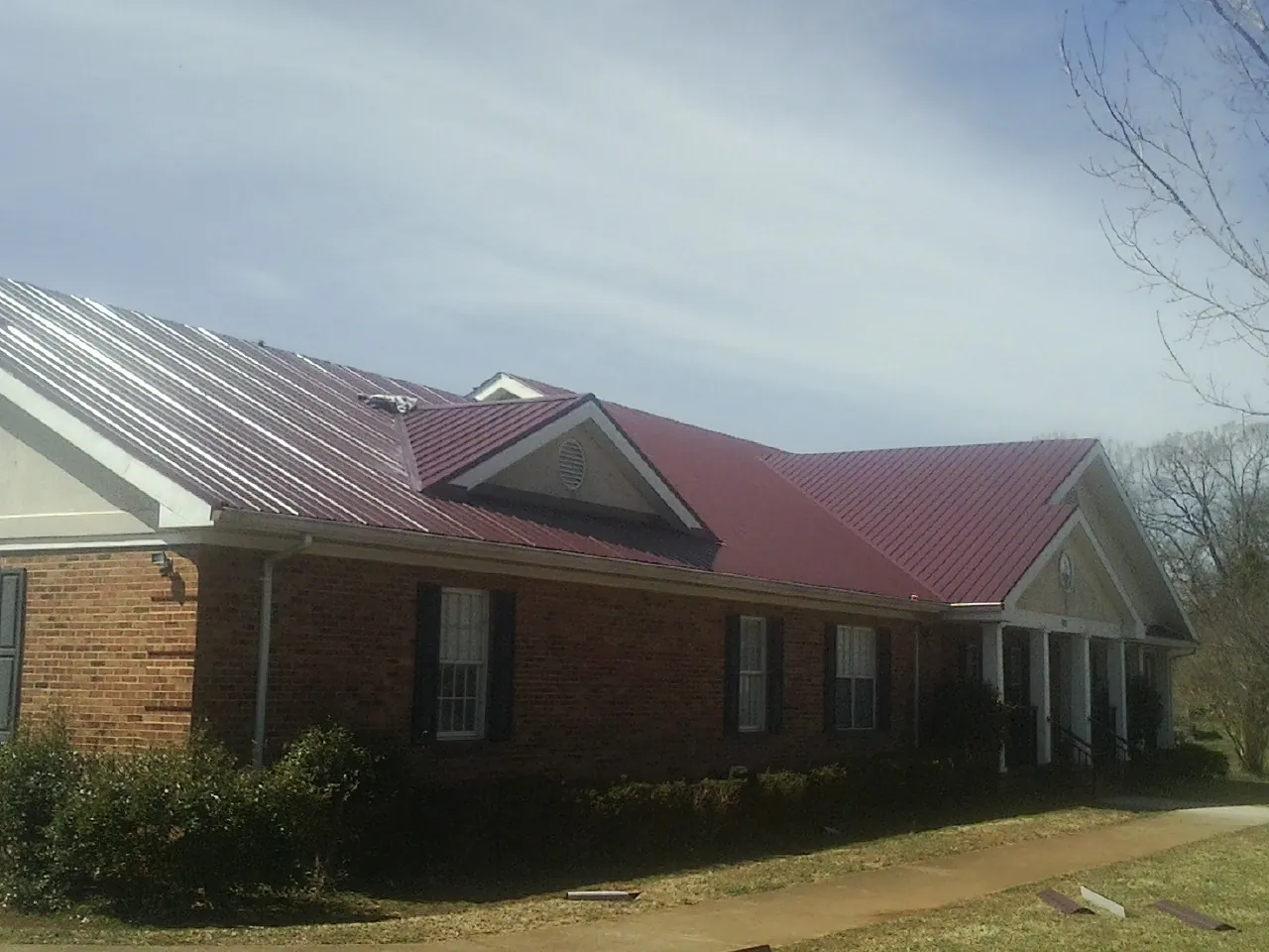 Red metal roof with gabled entries on a long brick building, from a Hail Damage Roof Repair job in Bird Island