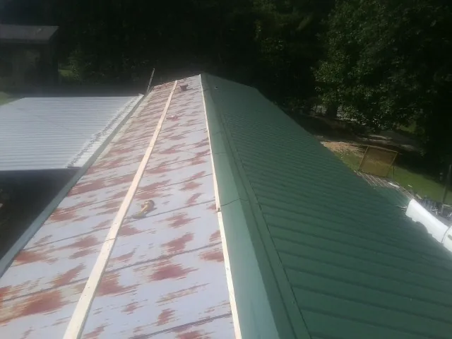 Old rusted panels beside newly installed green metal roofing — Wind Damage Roof Repair by Roofing Brothers in Bird Island