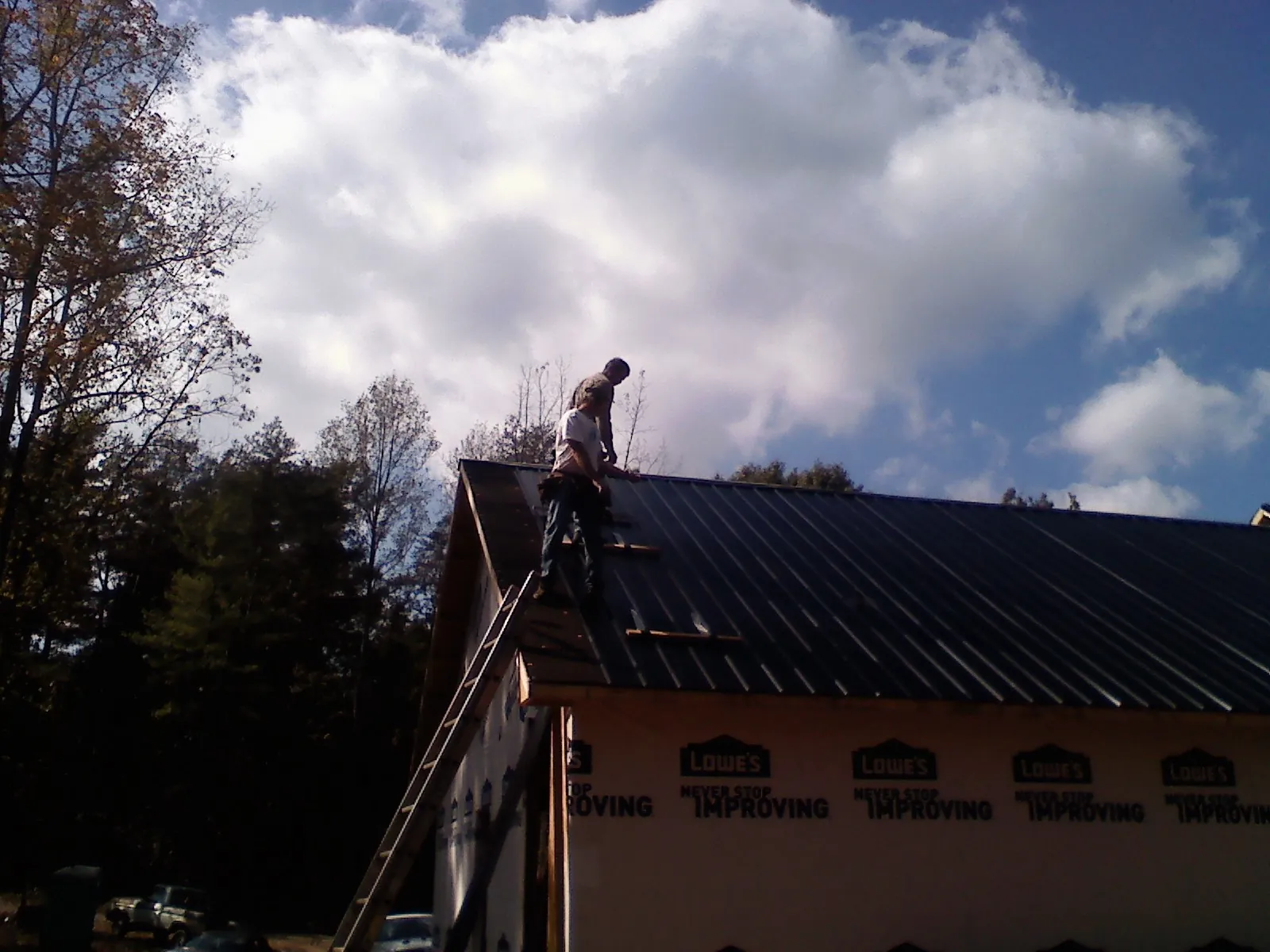 Roofer fastening dark metal panels high against a cloudy sky, from a Roof Inspection job in Bird Island