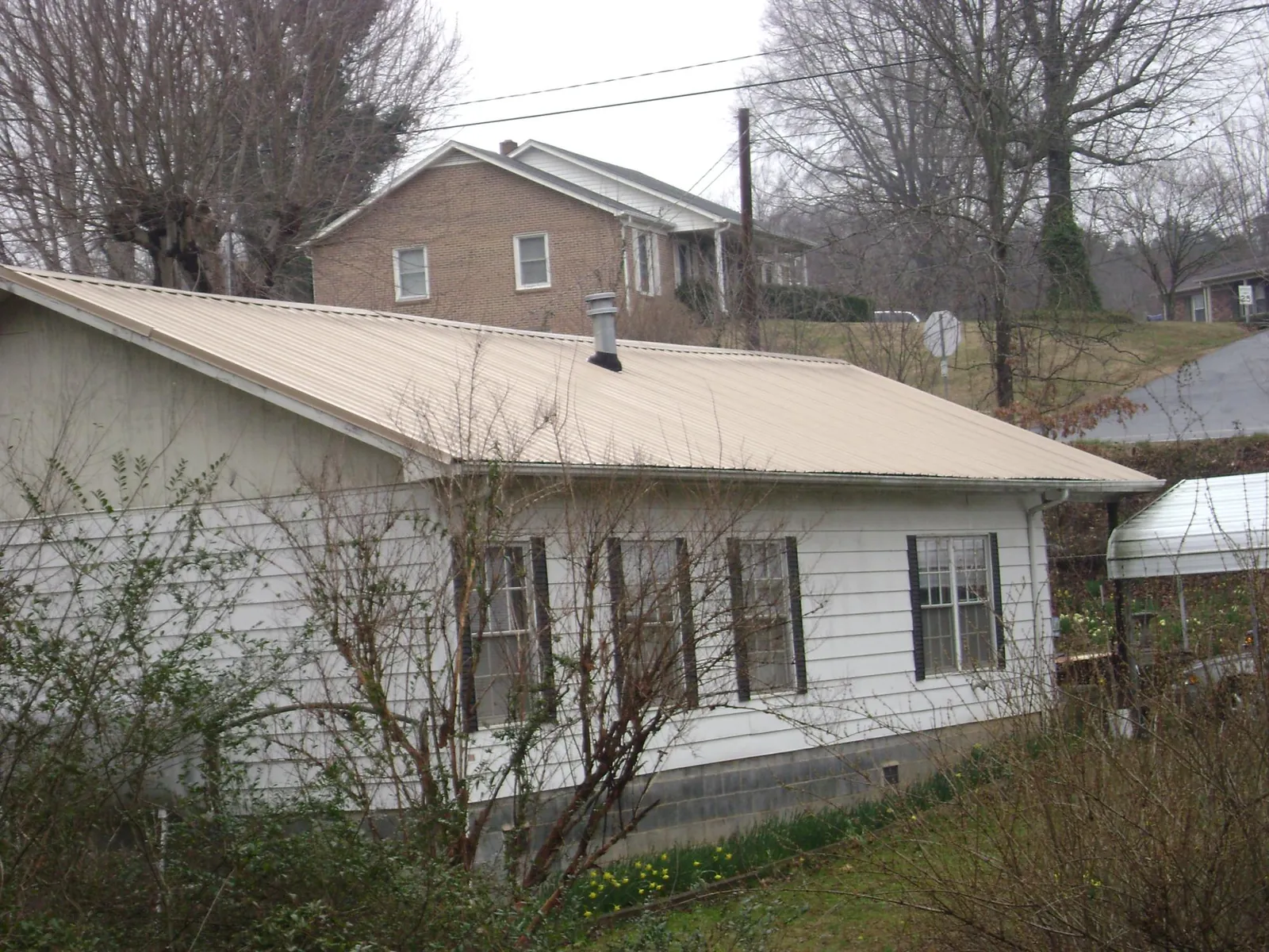 Tan metal roof on a white sided house set into a hillside — Commercial Roofing by Roofing Brothers in Bird Island